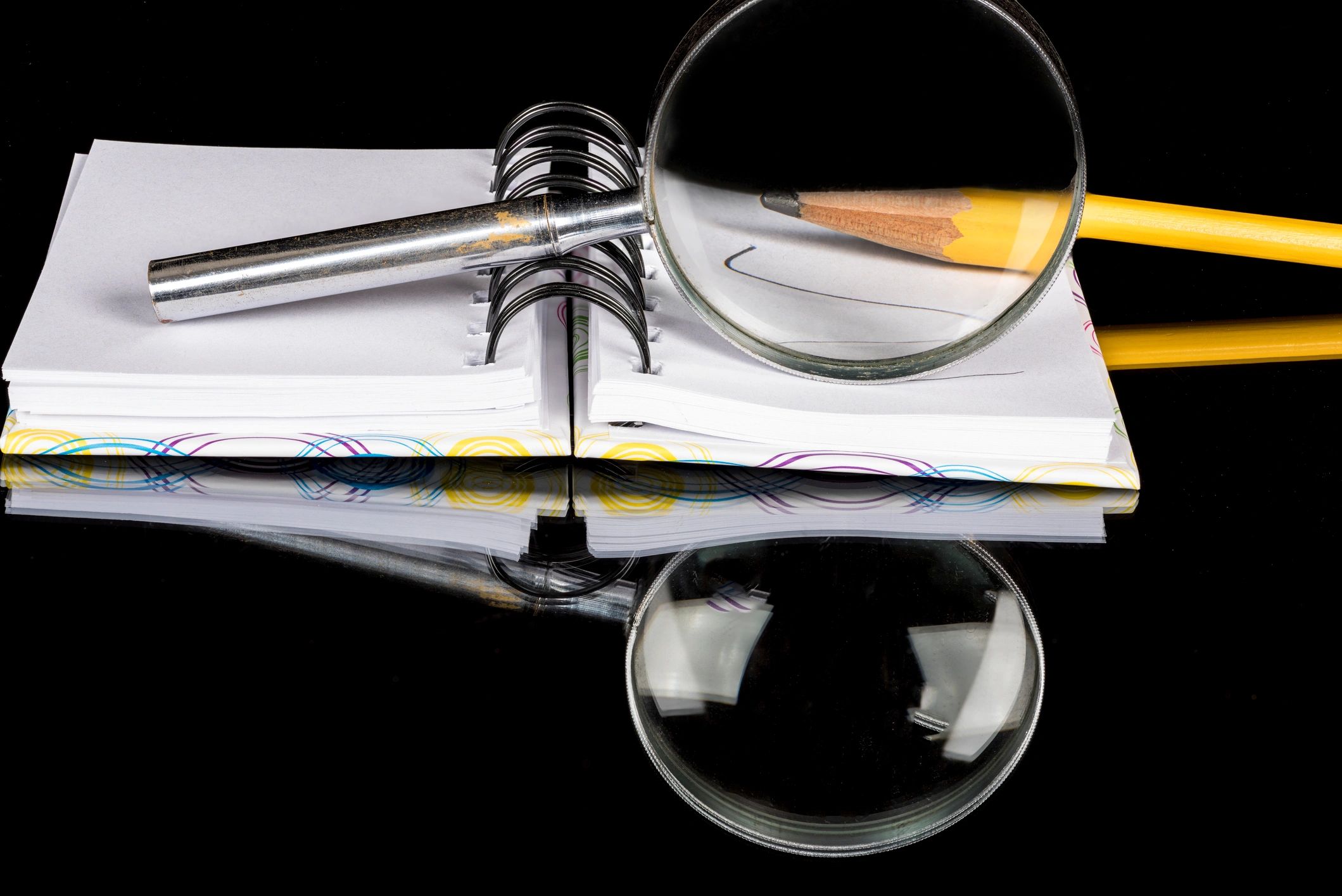 Close up of a magnifying glass and pencil with a pad of paper